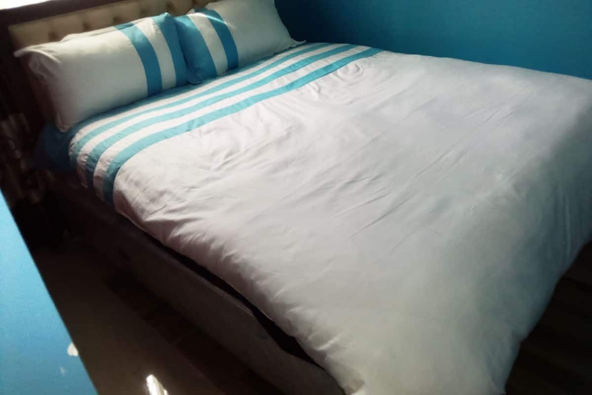 Una cama con ropa de cama a rayas blancas y azules, un cabecero de madera y una pared azul de fondo.