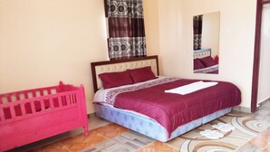 A bedroom with a bed, a pink crib, patterned curtains, and a mirror. - Eastward Garden Hotel (Nyahururu)