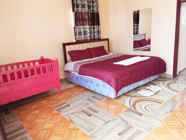 A bedroom with a bed, a pink crib, patterned curtains, and a mirror.