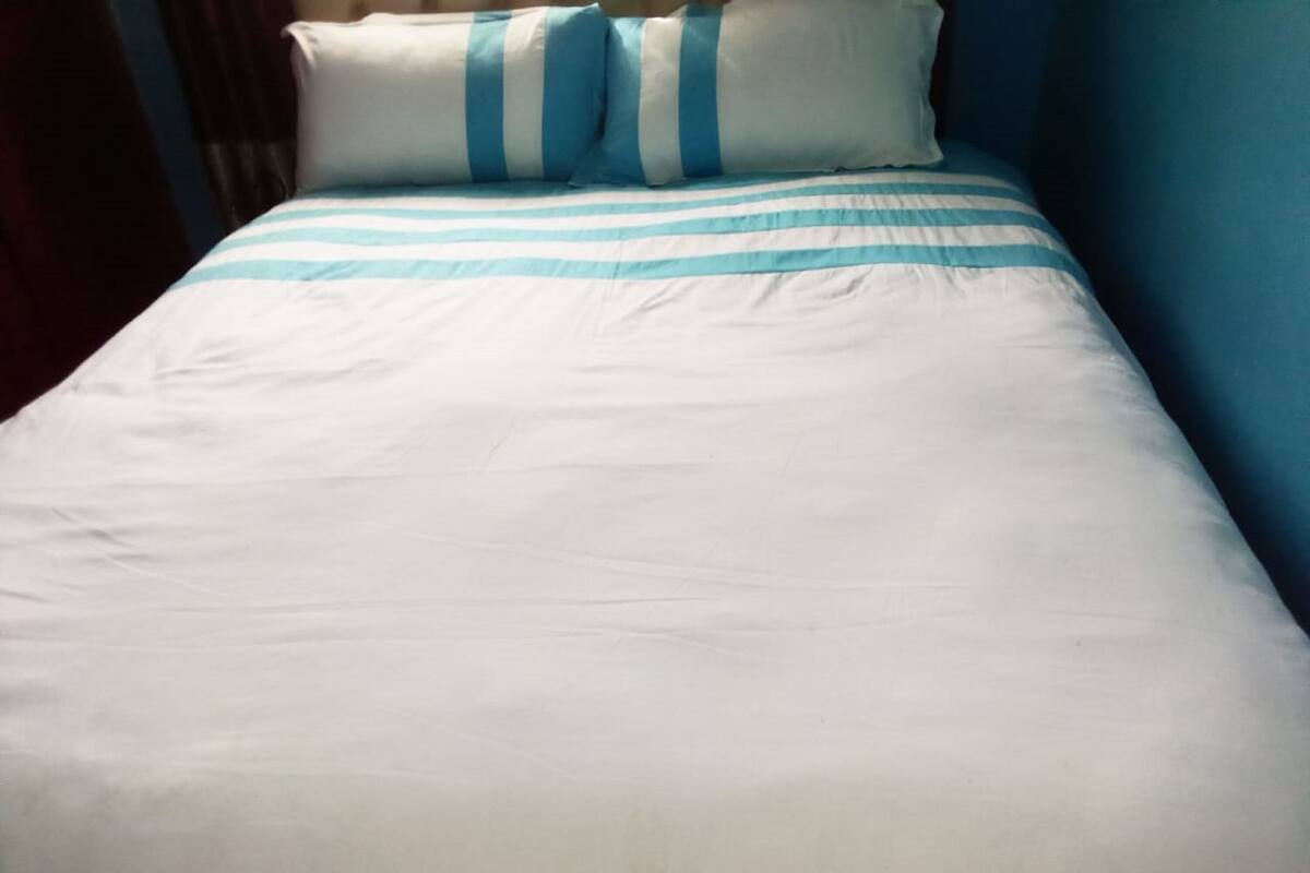 Una cama con ropa blanca a rayas azules, una almohada a rayas azules y una pared azul.