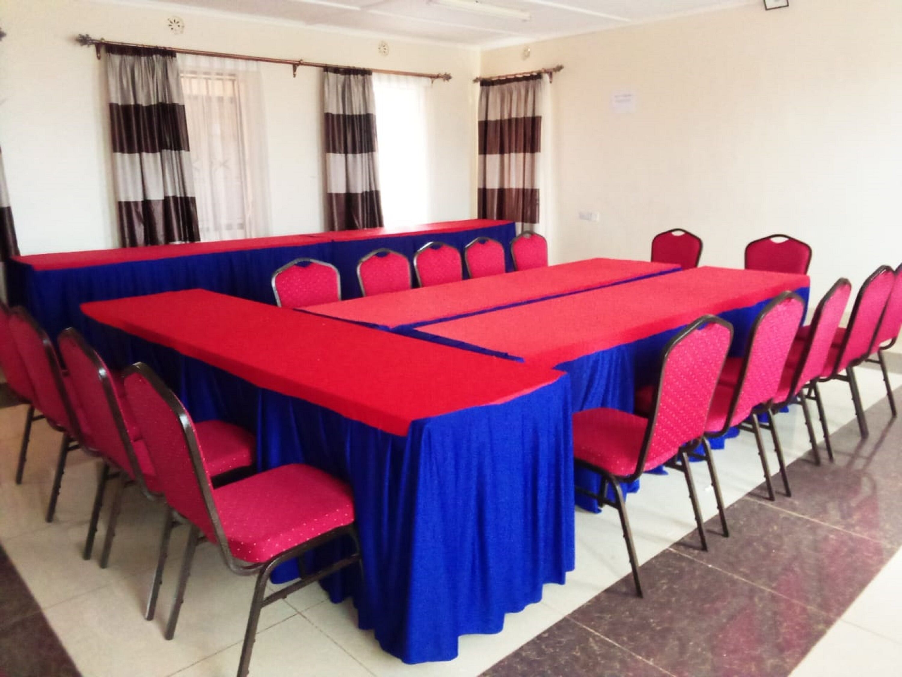 A conference room with a long table and chairs, red and blue tablecloths, and curtains on the windows.