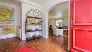 A room with a large map, a metal shelf with decorative items, a red door, and a tiled floor. - Malsac is a spacious holiday home with large garden and private swimming pool (Florimont-Gaumier)