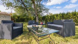 An outdoor seating area with wicker furniture and a glass table, surrounded by grass and trees. - Malsac is a spacious holiday home with large garden and private swimming pool (Florimont-Gaumier)