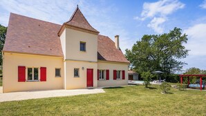 A two-story house with a red-tiled roof, a small tower-like structure, and a red door. - Malsac is a spacious holiday home with large garden and private swimming pool (Florimont-Gaumier)