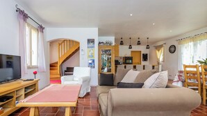 A cozy living room with a TV, sofa, and a small table. There's a staircase leading to another level, and a kitchen area with a microwave and cabinets. - Malsac is a spacious holiday home with large garden and private swimming pool (Florimont-Gaumier)