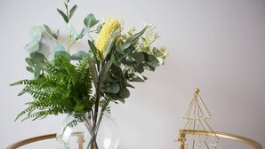 A clear glass vase with a variety of green plants and a small golden Christmas tree on a glass table. - Elegant 2br@footscray Station (Footscray)