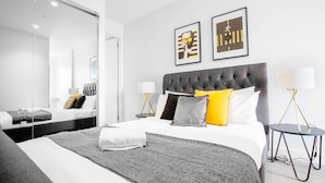 A modern hotel room with a large bed, a mirror, two framed artworks, and a bedside table with a lamp. - Elegant 2br@footscray Station (Footscray)