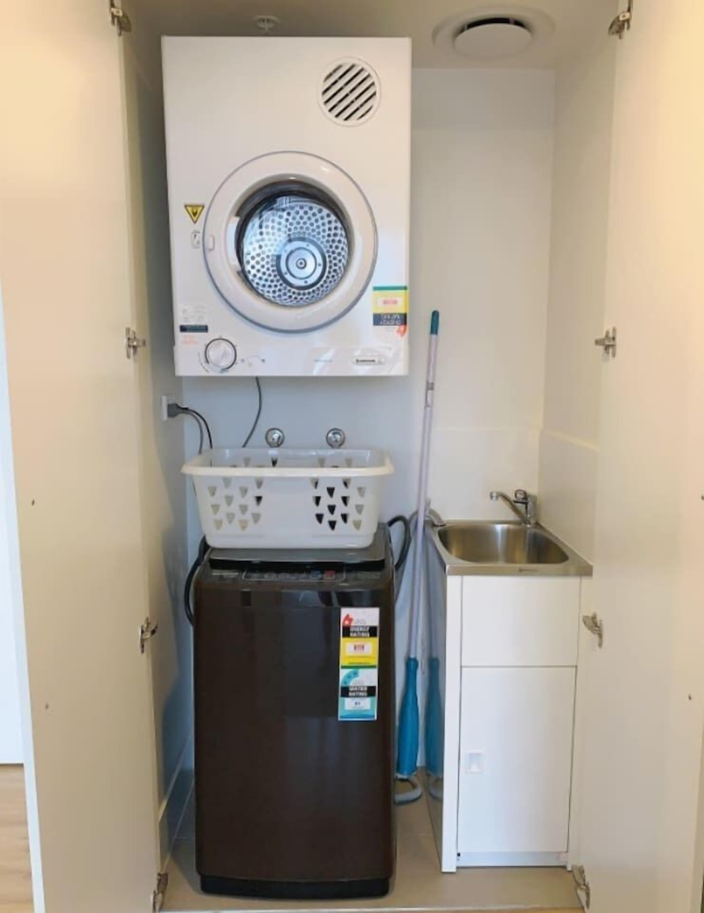 A compact utility room with a washing machine, a small sink, and a mop.