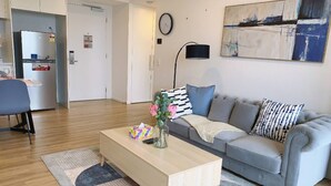 A modern living room with a grey sofa, a wooden coffee table, and a dining area with a chair and table. - Surferparadise Gem+parkingflexible Refund (Surfers Paradise)