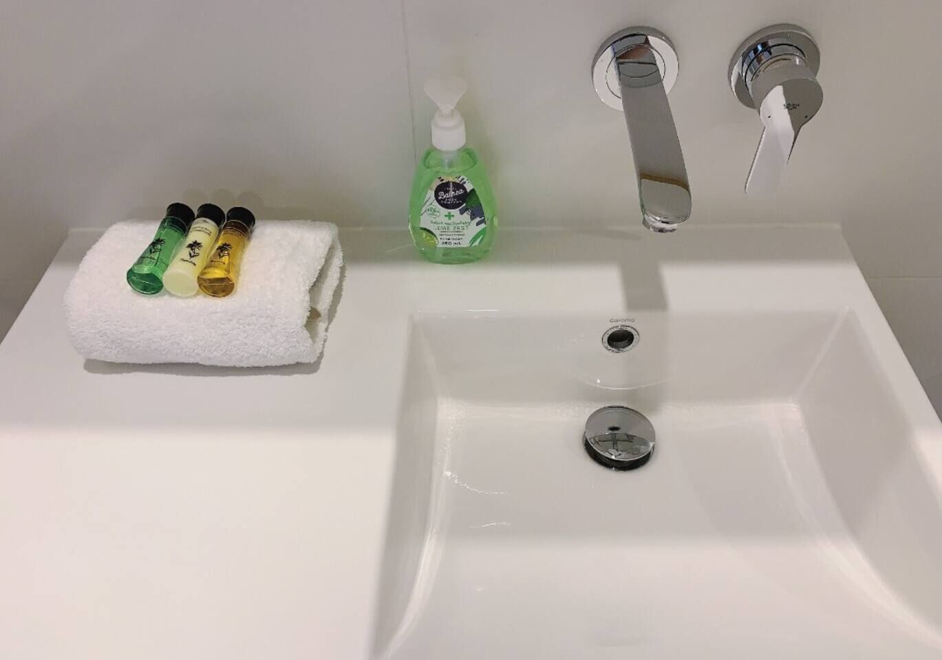 Een badkamer met een wit wastafelblad, een handdoek en vier flessen handzeep.