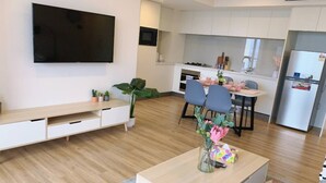 A modern living room with a flat-screen TV, a wooden coffee table, and a dining area with chairs and a table. - Surferparadise Gem+parkingflexible Refund (Surfers Paradise)