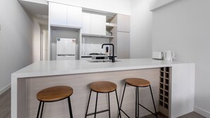 A modern kitchen with white cabinetry, a central island with stools, and a built-in wine rack. - Delightful Townhouse Stay@moonee Ponds + Parking (Moonee Ponds)