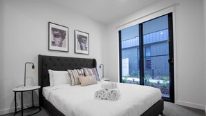 A modern bedroom with a large bed, a side table, a reading lamp, and a window with a view of a brick building. - Delightful Townhouse Stay@moonee Ponds + Parking (Moonee Ponds)