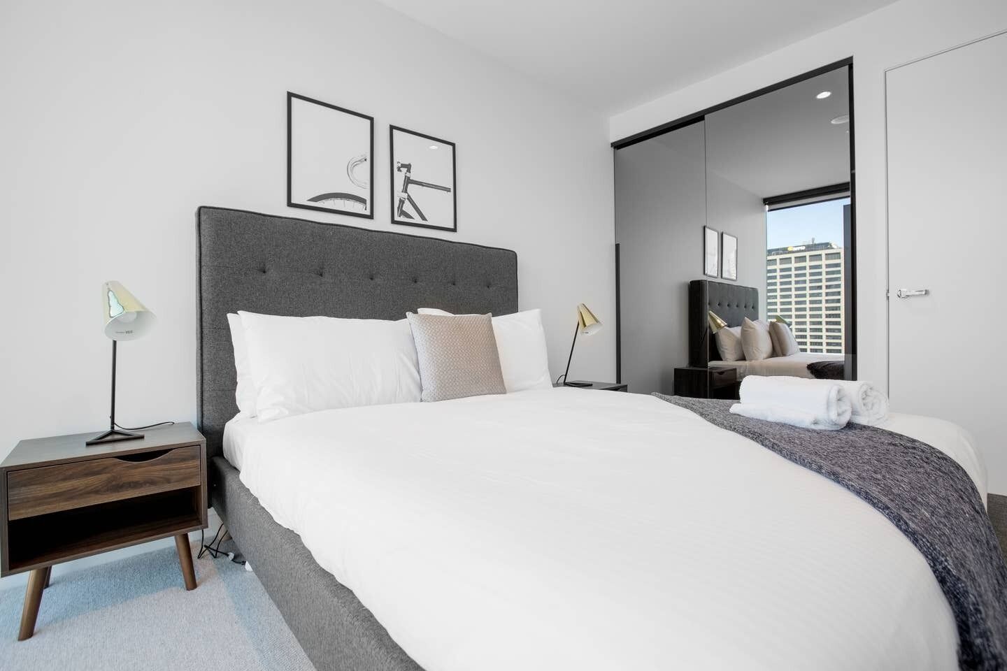 A modern hotel room with a large bed, a nightstand, a desk, and a mirror.