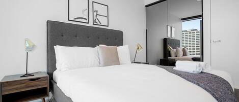 A modern hotel room with a large bed, a nightstand, a desk, and a mirror.