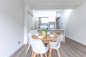 Une cuisine moderne avec des meubles blancs, un îlot central et un coin repas comprenant une table ronde et des chaises blanches.