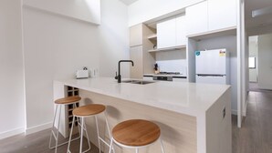 A modern kitchen with a central island, bar stools, a built-in oven, and a refrigerator. - Elegant Stylish Living@mooneeponds Wifi/parking (Moonee Ponds)