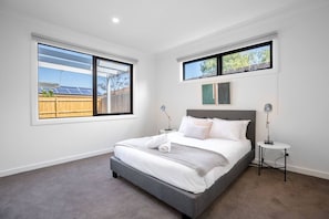 Une chambre moderne avec un grand lit, deux tables de chevet et une vue sur un jardin avec des panneaux solaires.
