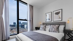 Una camera d'hotel moderna con un ampio letto, vista sulla città e due quadri appesi alla parete.