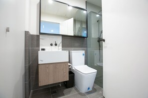 Een moderne badkamer met een wit toilet, een houten wastafelmeubel, een spiegel boven de wastafel en een douchehoek.