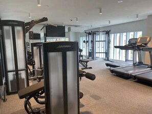 Een fitnessruimte met cardioapparatuur, krachttrainingsmachines en een loopband.