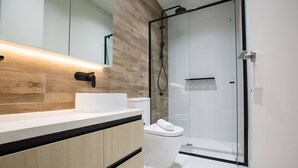 A modern bathroom with a wooden vanity, a glass shower enclosure, and a white toilet.