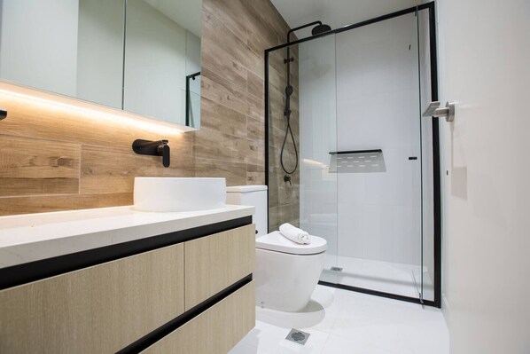 A modern bathroom with a wooden vanity, a glass shower enclosure, and a white toilet.