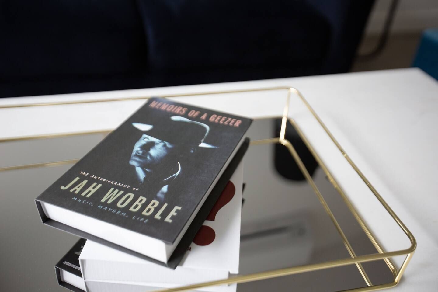 A book titled "Memoirs of a Geezer" by Jah Wobble on a white table with a gold frame.