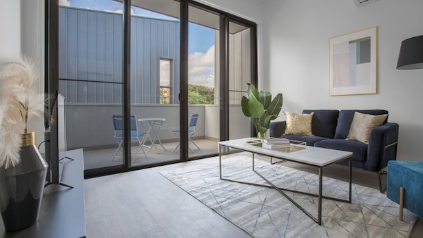 A modern living room with a sofa, coffee table, and a view of a blue building through large glass doors.
