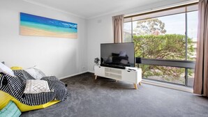 A modern living room with a large window, a flat-screen TV, and a cozy seating area with patterned cushions. - Sweethome2br@highton+parking (Highton)