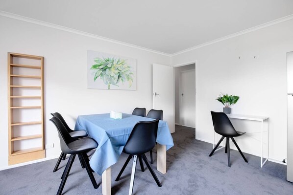 A modern dining area with a blue table, black chairs, a wooden ladder, a potted plant, and a painting on the wall.
