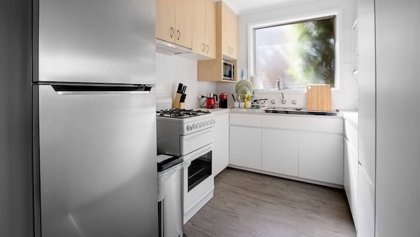 A modern kitchen with a stainless steel refrigerator, a gas stove, and white cabinetry. - Sweethome2br@highton+parking (Highton)