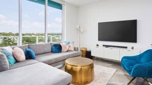 A modern living room with a grey sofa, a blue chair, a gold side table, and a large TV on the wall.