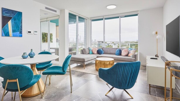 A modern living room with a large window, a sofa, a coffee table, and a dining area with chairs and a table.