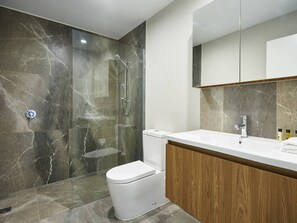 A modern bathroom with a glass-enclosed shower, a white toilet, and a wooden vanity with a sink.
