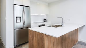 A modern kitchen with a stainless steel refrigerator, a built-in oven, a coffee maker, and a wooden countertop island with a sink.