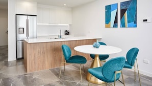 A modern kitchen with white cabinets, a central island, and a round table with teal chairs.