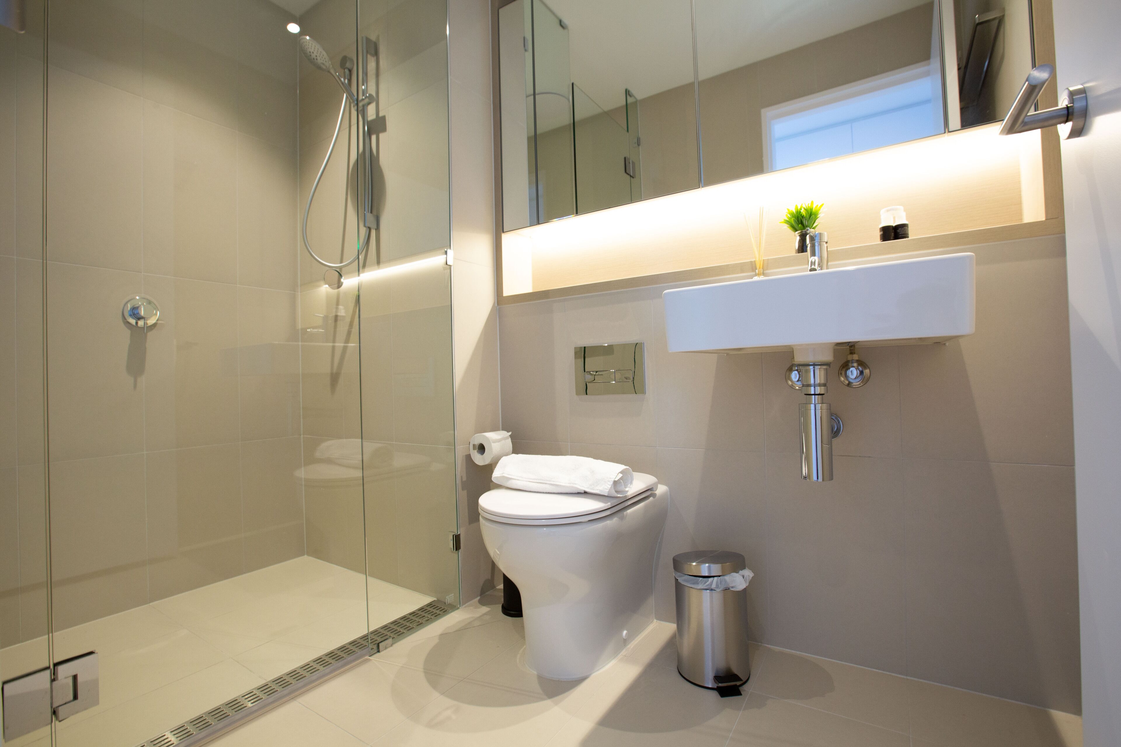 A modern bathroom with a glass-enclosed shower, a toilet, a sink, and a trash can.