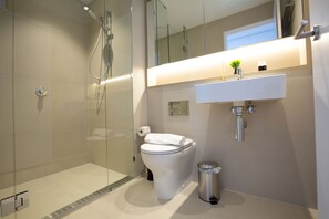 Une salle de bain moderne avec une douche à parois de verre, des toilettes, un lavabo et une poubelle.