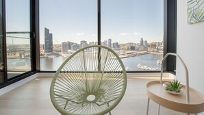 A modern room with a large window, a green chair, a small table with a plant, and a city view. - Central Melbourne 2br2bt APT on Collins St+parking (Docklands)