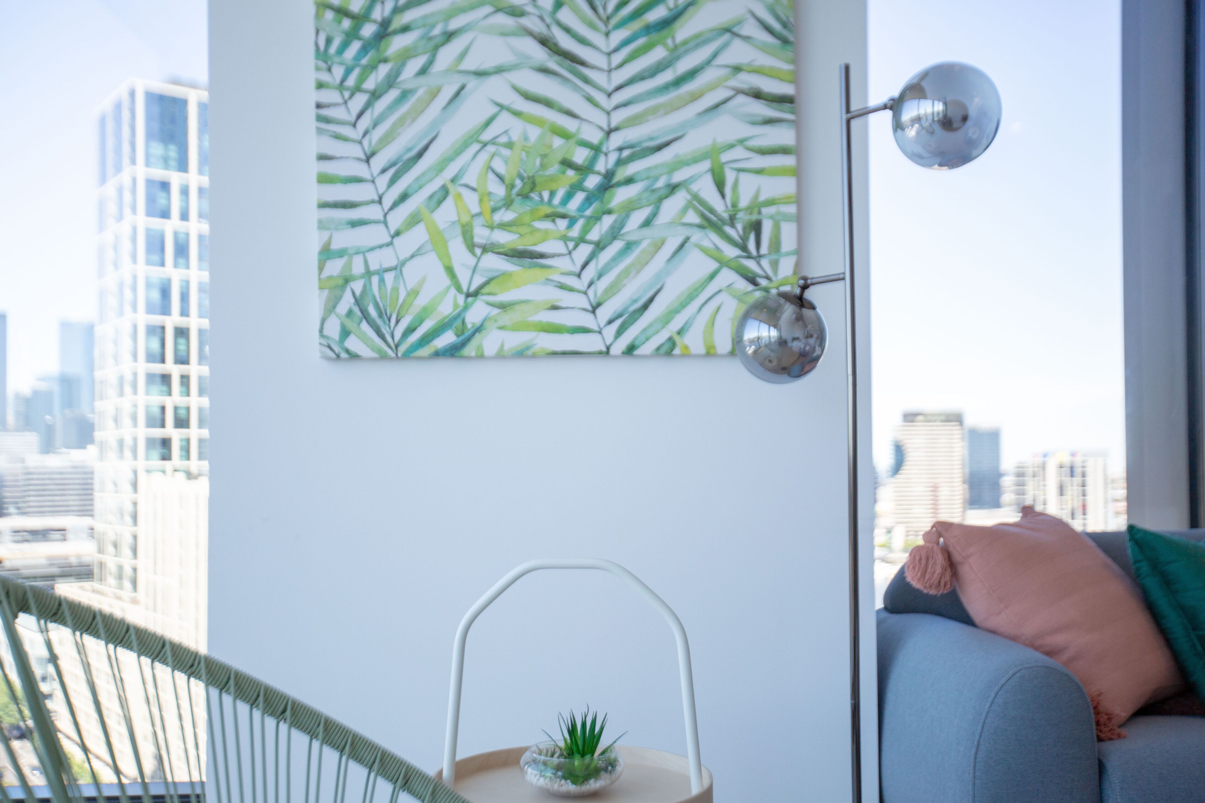 Sala moderna com vista para a cidade, uma pequena planta sobre uma mesinha lateral e um sofá com almofada.