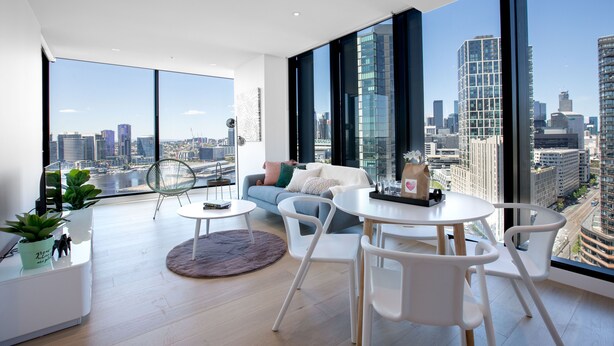 A modern living room with a city view, featuring a sofa, chairs, a dining table, and a large window. - Central Melbourne 2br2bt APT on Collins St+parking (Docklands)
