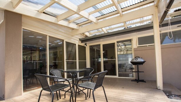 Eine Außenpatio mit Glastür zu einem Innenraum, einem runden Tisch mit Stühlen und einem Grill.