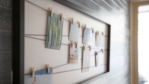 Eine Wand mit einem gerahmten Kunstwerk, das aus mehreren kleineren Teilen besteht, die jeweils mit Holzclothespins befestigt sind.