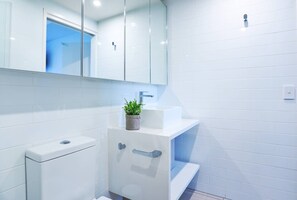 A modern bathroom with white tiles, a white sink, a mirror, and a potted plant. - Ultimate Prestige 2bed2bath Hamiltonapt (Hamilton)