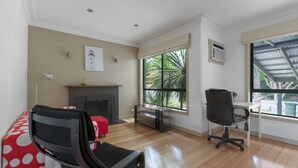 A modern living room with a fireplace, a large window with a view of greenery, a black office chair, and a red polka dot sofa. - Spacious 3bedrooms big House@mitcham (Mitcham)
