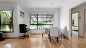 A spacious room with a large window, a black office chair, a round table with white chairs, and a wooden floor. - Spacious 3bedrooms big House@mitcham (Mitcham)