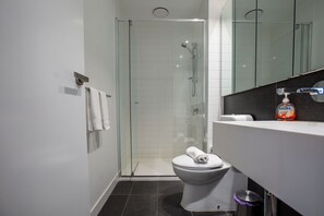 A modern bathroom with a glass-enclosed shower, a white toilet, and a black countertop with a soap dispenser.