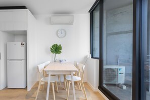 A modern kitchen with white cabinets, a white refrigerator, a clock on the wall, and a large window with a view of the outside.