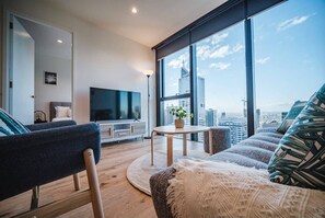 Una sala de estar moderna con una televisión grande, un sofá, una mesa de centro y vistas a la silueta urbana.